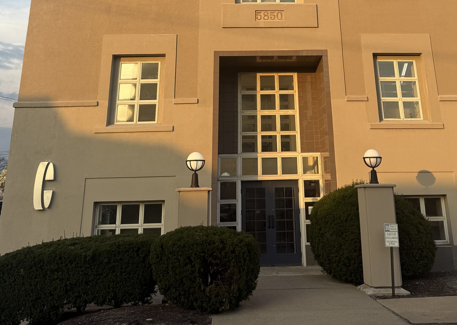 The main entrance at 5850 Ellsworth Avenue: glass double doors under the 5850 stone sign, between two globe lamps.